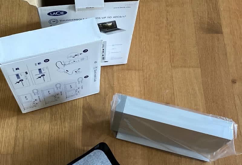 Photo: opened box of the LaCie d2 Thunderbolt 3 external hard drive, showing the hard drive and the inner box, which contains the connection cable and power supply unit and on the lid of which the quick start guide is printed.